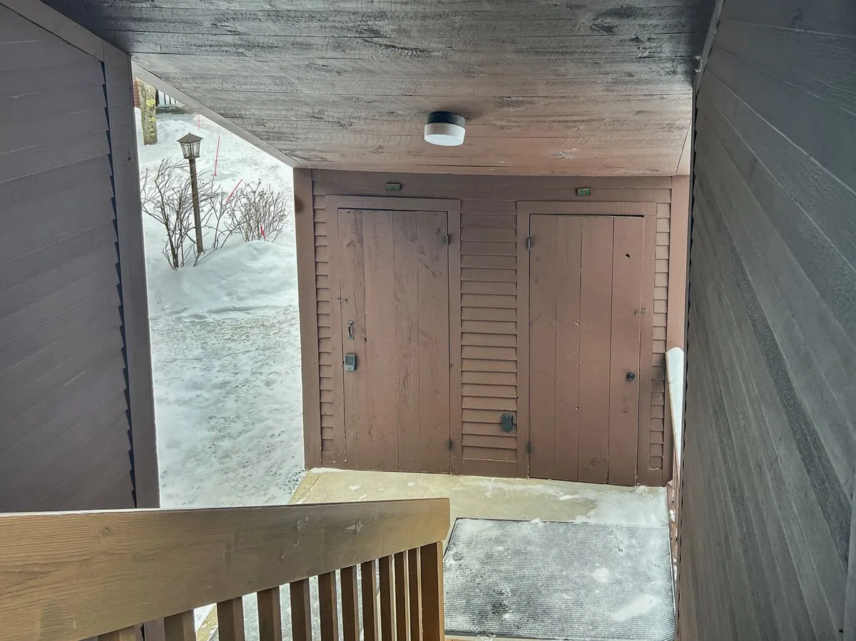 This image features a cozy entryway with a visible staircase, two doors, and an overhead light. The area conveys a welcoming transition zone designed for entering the property and storing outdoor gear after a day on the slopes.