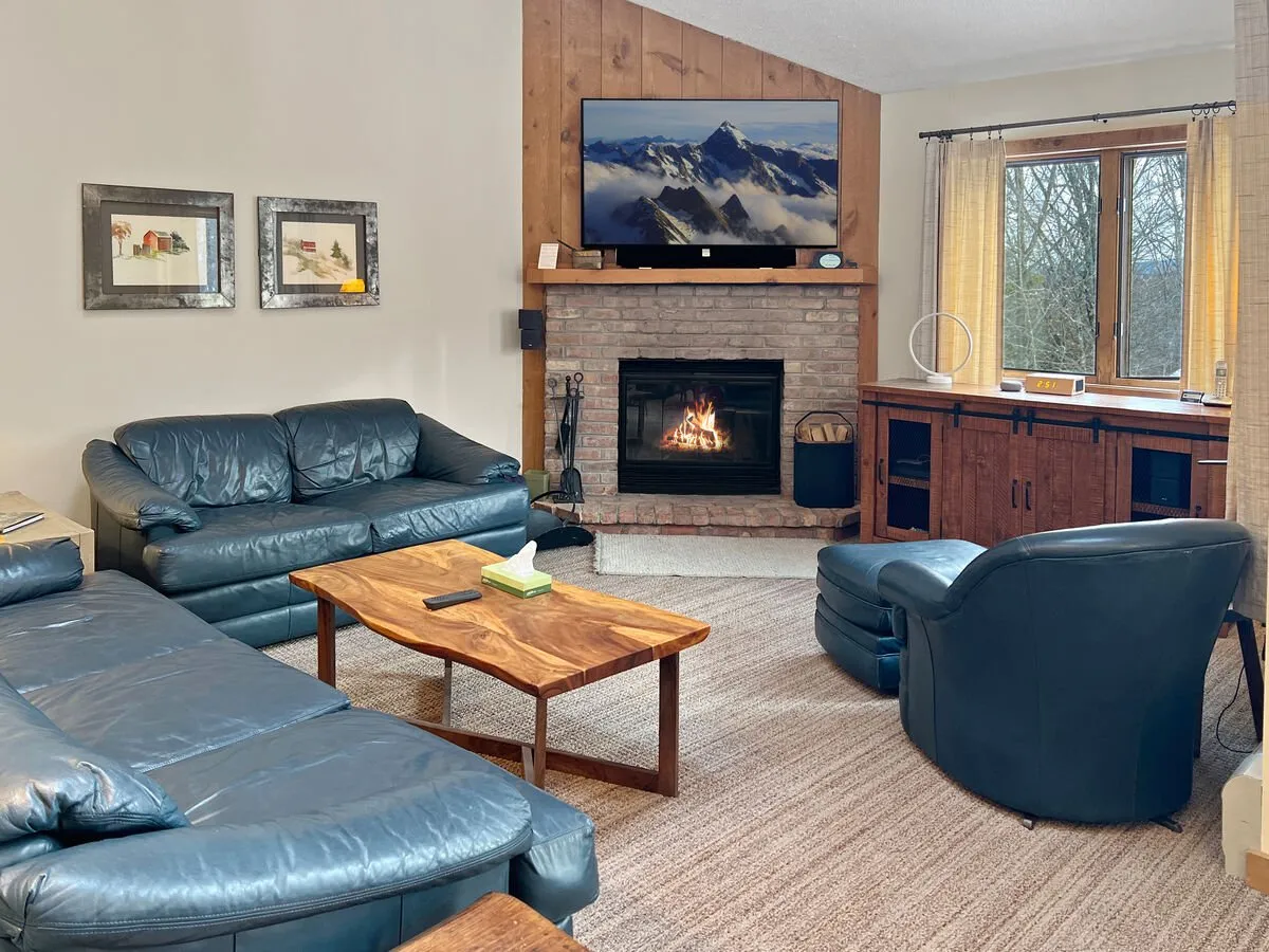 A cozy living area centered around a fireplace, with plush leather sofas, a wooden coffee table, and a television. The ambiance is warm and perfect for family gatherings or relaxing movie nights.