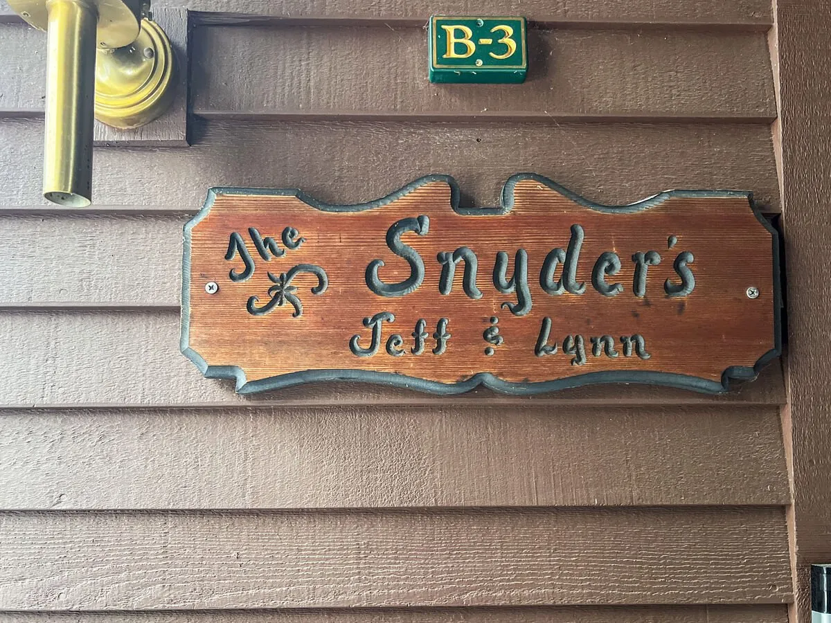 This interior shot features a personalized sign with the family name 'Snyder's' and the names 'Jeff & Lynn' illuminated by a brass light fixture, creating a welcoming entryway or gathering point. The scene radiates a homey, family-oriented vibe ideal for welcoming both families and friend groups.