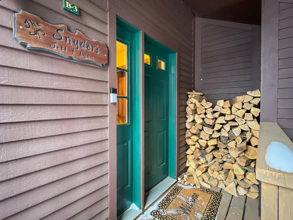 An inviting entrance scene showing a woodpile, green doors, and clear signage. The setting is perfect for welcoming guests coming in from the cold and suggests a functional area for gear drop-off and organization.