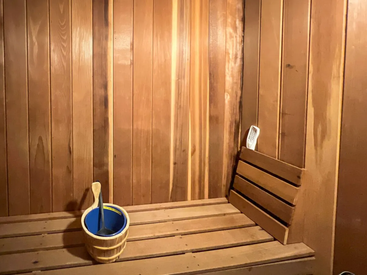 A tranquil sauna interior, featuring wooden walls, a sauna bench, and a bucket with a ladle. The warm wood tones and soft lighting create a spa-like atmosphere, ideal for relaxation and rejuvenation.
