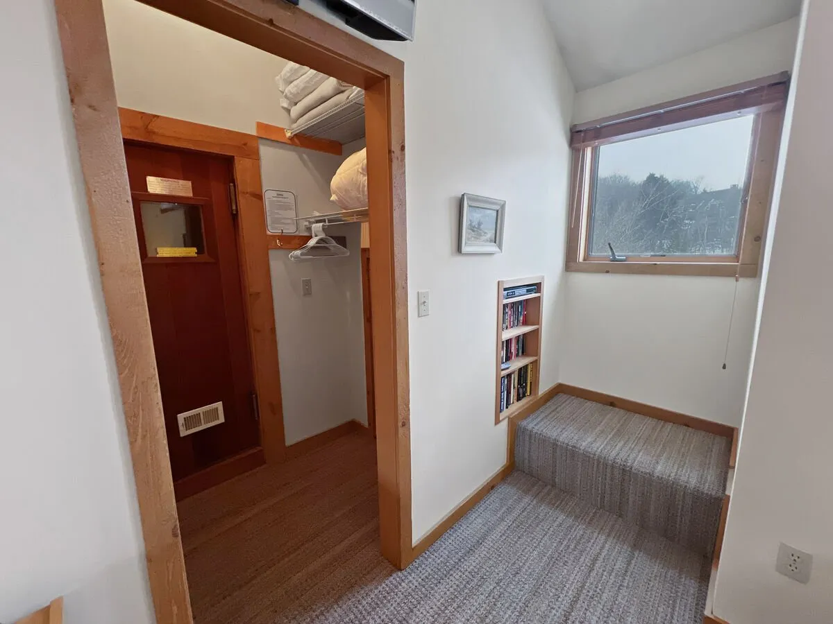 An inviting staircase area with a bookshelf and a window that offers a glimpse of the outdoors, creating a welcoming transition space. The area feels organized and functional, with natural light enhancing the inviting mood.