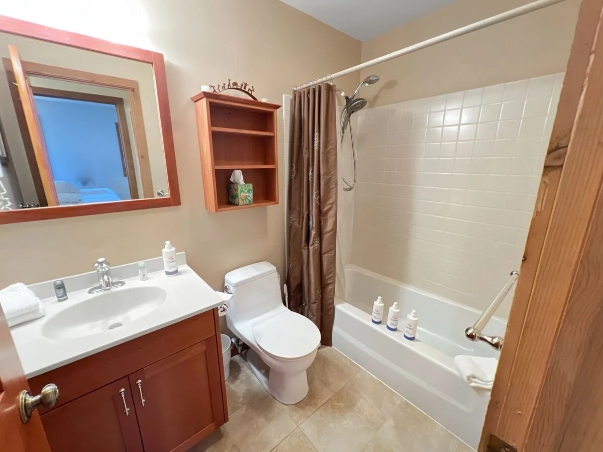 A bright, functional bathroom with a sink, mirror, and shower—accentuated by thoughtful details like a shelf for toiletries and a soft shower curtain. The mood is practical yet inviting, suggesting opportunities for personal relaxation after adventure.