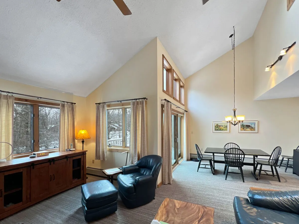 The scene captures a cozy dining area with a generous table surrounded by comfortable chairs and large windows that fill the space with natural light. The adjoining wooden bar subtly references the kitchen just beyond. The ambiance is perfect for both family gatherings and casual meals, with a sense of openness that encourages togetherness.